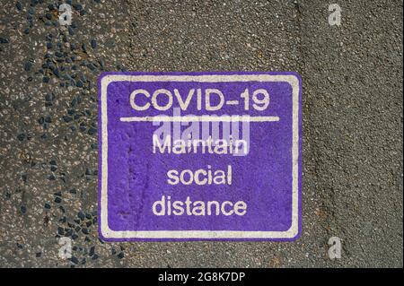 Purple COVID-19 social distancing sign painted on pavement or road. Stock Photo