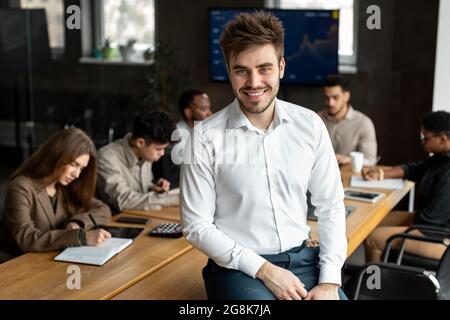 Smiling young businessman sitting on desk and posing Stock Photo