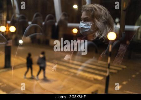 Blonde girl wearing face mask reflected in bus window at night, London, 21 February 2021 Stock Photo