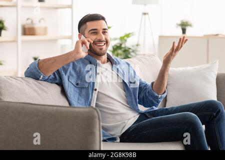 Portrait of smiling millennial man talking on phone at home Stock Photo