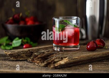 Cherry gin on a wooden table with cherries in the background Stock Photo