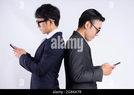 Young Vietnamese male employees in suits standing back to back and using phones Stock Photo