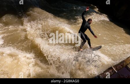 Munich, Germany. 21st July, 2021. A man rides the Eisbach wave in the English Garden. The artificial wave is considered a popular hotspot for surfers and spectators all year round. Credit: Peter Kneffel/dpa/Alamy Live News Stock Photo