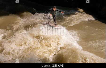 Munich, Germany. 21st July, 2021. Australian-born Murray Keegan rides the Eisbach wave in the English Garden. The artificial wave is considered a popular hotspot for surfers and spectators all year round. Credit: Peter Kneffel/dpa/Alamy Live News Stock Photo