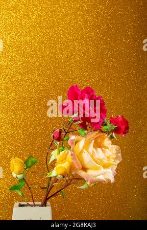 Photo of some beautiful natural red and yellow roses in a handmade vase on a gold colored textured background.The photography has copy space to make a Stock Photo