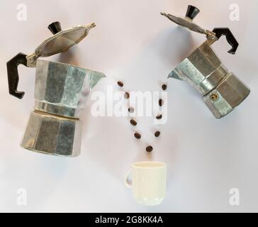 Roasted coffee beans come out of two vintage coffee machines into a white cup Stock Photo