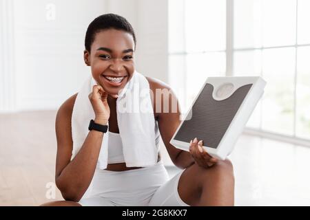 Happy African Woman Holding Bathroom Scales. Slimming Stock Photo