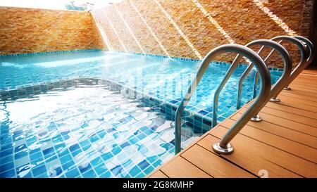 An empty turquoise swimming pool with grab bars ladder at sunrise. Focus on grab bars ladder. Stock Photo