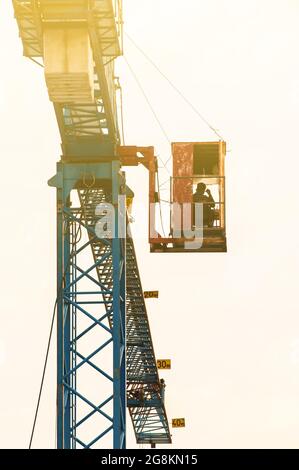 An Asian man crane operator climbs the crane ladder of the old hammerhead crane to the control cabin at a construction site. Focus on the crane. Stock Photo