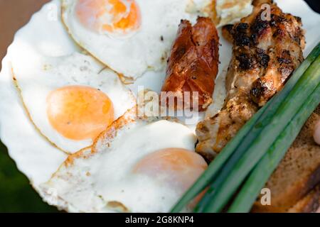 Spring omelette with bacon, green onion, Fried egg grilled sausages, BBQ meat, herbs served with homemade rustic bread for breakfast in countryside. F Stock Photo