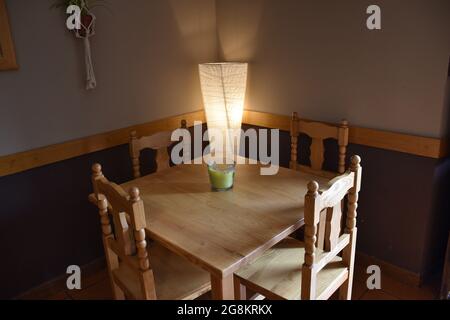 Twilight restaurant table with lit paper lamp. Table, four chairs and green candle on the table, natural light coming from the right. Stock Photo