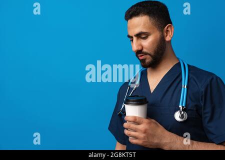 Young arab doctor drinking cup of coffee standing over blue background Stock Photo