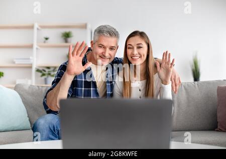Cheerful mature couple calling their friends on webcam, talking to family remotely from home, waving at camera Stock Photo
