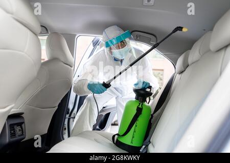 Specialist cleaner wearing personal protective equipment PPE using chemical alcohol spray Stock Photo