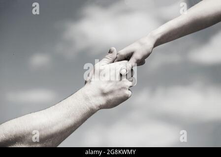 Solidarity, compassion, and charity, rescue. Giving a helping hand. Hands of man and woman on blue sky background. Lending a helping hand. Black and Stock Photo