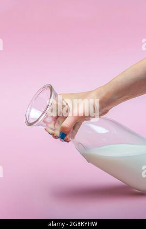 A jug of milk on a pink background in a woman's hand. Milk in a glass bottle. Space for text, large banner. Stock Photo