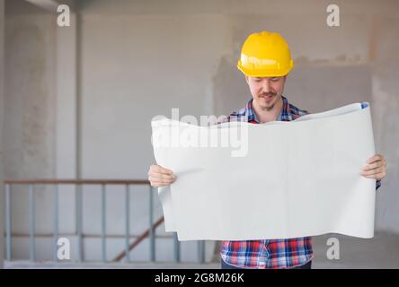 Caucasian engineer holding and reading plan on blueprint in construction site. There is copy space on the left. Stock Photo