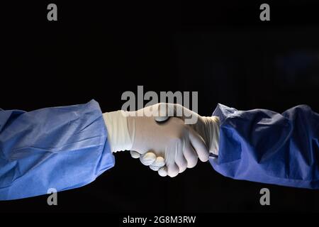 Two doctors in surgery cloth with rubber gloves shaking hands with team confident before start to do cure operation in dark surgery room. Stock Photo