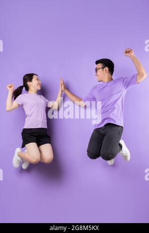 Young Vietnamese students happily jumping and giving high five on vibrant purple background Stock Photo