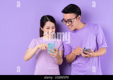 Young Vietnamese friends happily using their smartphones on vibrant purple background Stock Photo