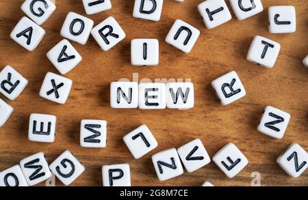 Small white and black bead cubes on wooden board, letters in middle spell NEW Stock Photo