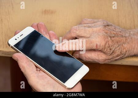 Elderly senior woman holding white mobile phone in her hands, closeup detail Stock Photo