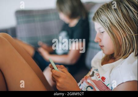 Alienation addiction. Two teenagers at home use their smartphones for social media. The concept of children's dependence on phones, social networks an Stock Photo