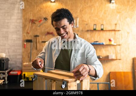 Carpenter measuring a wooden box and looking at his working drawings in workshop Stock Photo