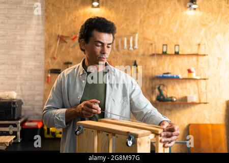 Carpenter measuring a wooden box and looking at his working drawings in workshop Stock Photo