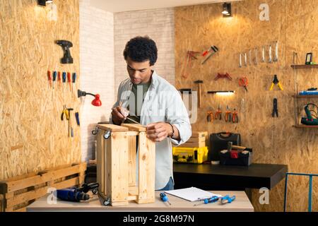 Carpenter measuring a wooden box and looking at his working drawings in workshop Stock Photo