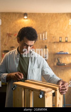 Carpenter measuring a wooden box and looking at his working drawings in workshop Stock Photo