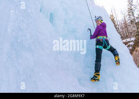 Female ice climber going down an ice waterfall, using a safety top rope. Stock Photo