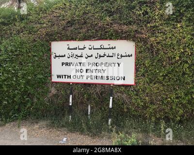 White Billboard of ''private property no entry without permission'' with white background over an Green fence and written in both English and Arabic w Stock Photo