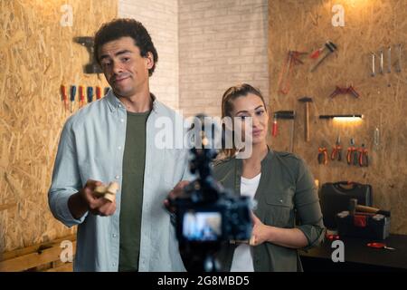 Two people in front of the camera on the set for a DIY blog in a carpentry workshop. The carpenters are explaining the creation process of wooden toys Stock Photo