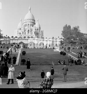 1950s, historical, two parisian ladies in coats and hats sitting on chairs on ground below the steps leading up to the famous french landmark, the domed Roman Catholic church, Sacre-Coeur, which sits on a hilly peak in Montmartre, Paris, France. Stock Photo