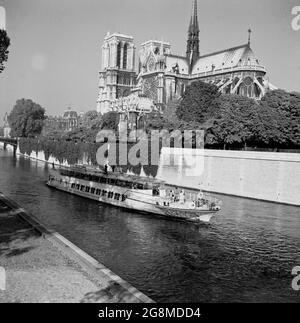 1950s, historical, a sightseeing pleasure cruise boat travelling on the river Seine going past the famous Notre-Dame Cathederal, Paris, France, A medieval Catholic church on the IIe de la Cite in the 4th arrondissement ofthe city, it is considered one of the finest examples of French Gothic architecture. Stock Photo