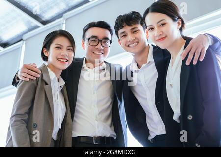Young Vietnamese business team in suits hugging each other in the office Stock Photo