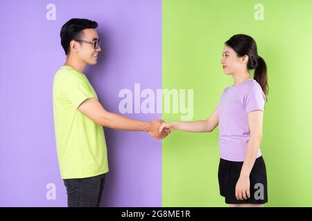 Young Vietnamese people shaking hands on green and purple split background Stock Photo