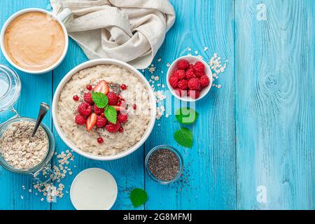 Oatmeal with raspberries, red currants, strawberries and chia seeds on a bright blue background. Top view, copy space. Stock Photo