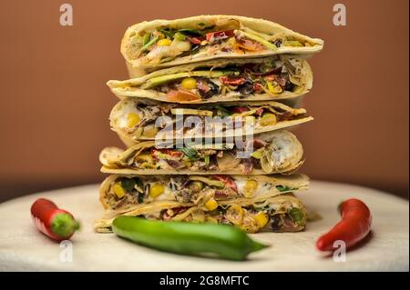 Beautiful closeup view of delicious creamy black bean Mexican quesadillas with sweet corn, avocado, red onion and coriander on wooden serving board Stock Photo