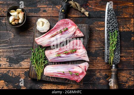 Raw lamb shanks meat on a cutting board with herbs. Dark wooden background. Top view Stock Photo