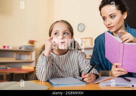 teacher with book looking at thoughtful girl in montessori school Stock Photo
