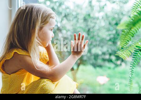 5 years old blonde girl staring out of the window on a wet cold rainy day Stock Photo