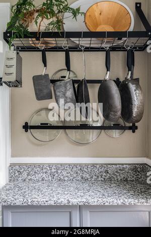 Vintage pots, pans, and skillets hanging from a kitchen rack over the counter