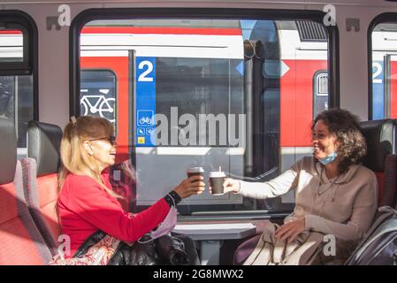 Happy women traveling by train making a toast with coffee and having fun. Stock Photo