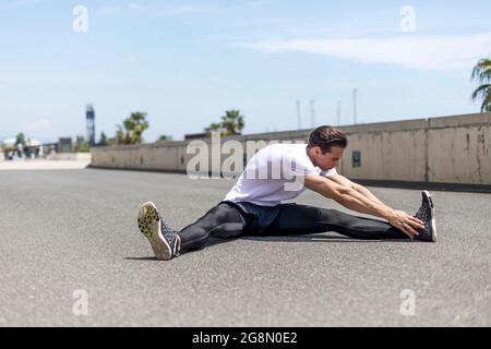 Portrait of sitting runner male outside doing stretch in street Stock Photo