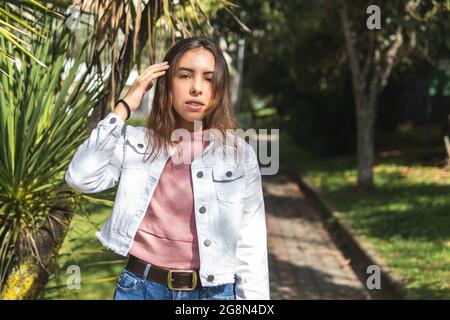 Portrait of a Latina teenage girl with straight hair and braces wearing a pink blouse looking at camera outdoors in a park Stock Photo