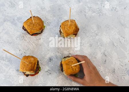 Overhead view of a hand taking a mini burger from a group of four Stock Photo