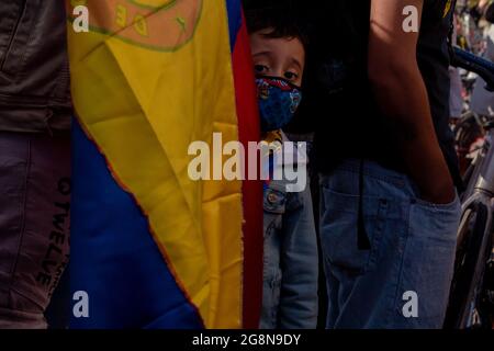 A small kid seen behind a Colombian flag during a new day of anti-government protests during the 211 celebration of Colombia's independence from spain, protests raised into clashes in various cities after intervention by Colombia's riot police ESMAD, in Bogota, Colombia on July 20, 2021. Stock Photo
