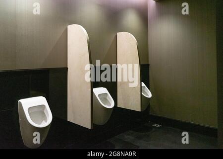 Three white men's urinals in a bathroom in lobby of luxurious hotel. Stock Photo